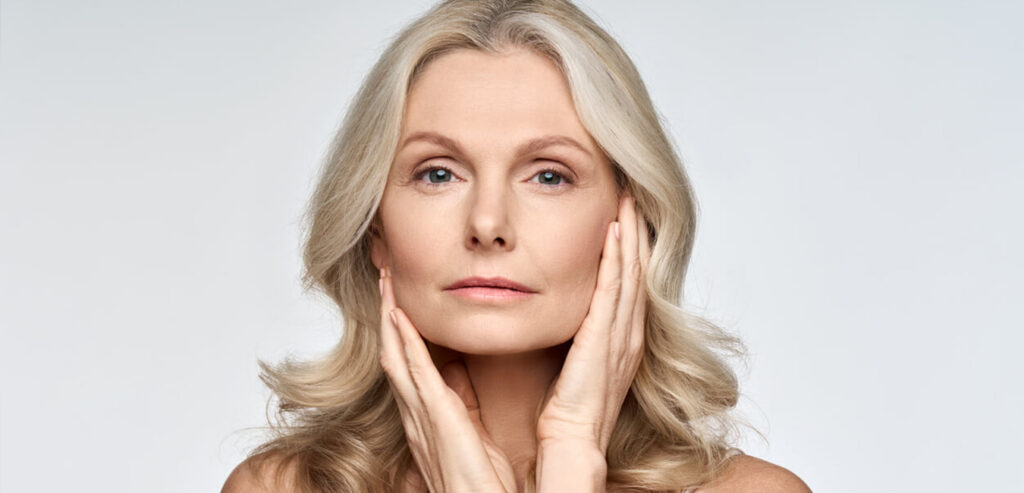 Mulher branca de meia idade com a mão no rosto após a aplicação de ácido hialurônico
